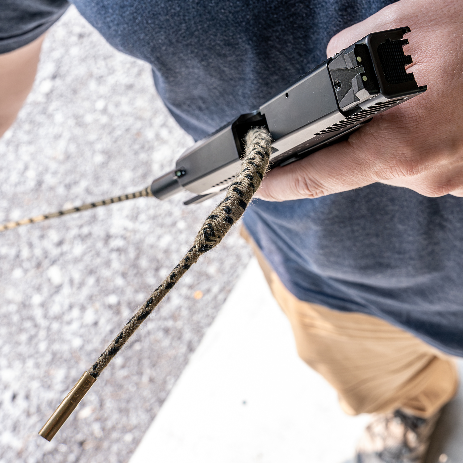 Person reinigt Pistole mit Reinigungsschnur im Freien auf hellem Boden.