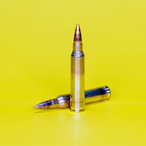 Zwei Gewehrpatronen stehen und liegen auf gelbem Hintergrund.