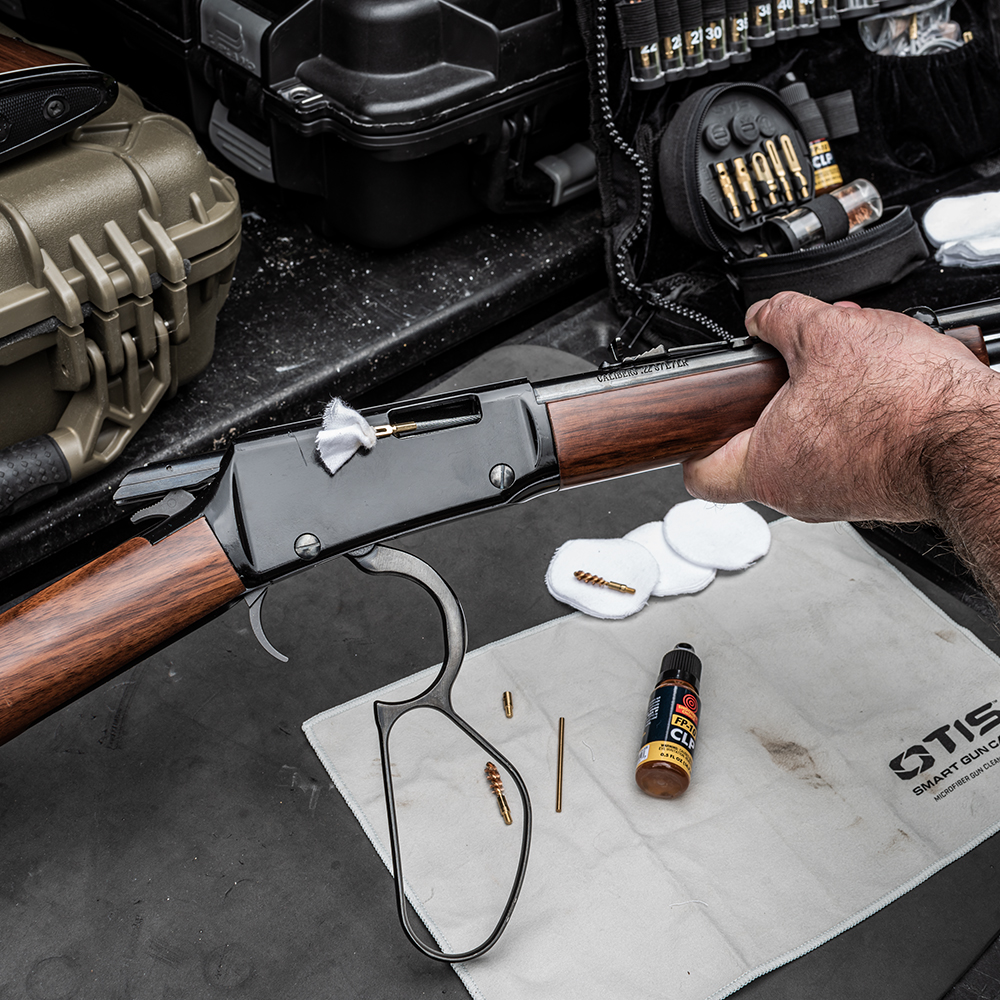 Gewehr wird gereinigt, umgeben von Reinigungsutensilien und Munitionskisten auf einer Werkbank.