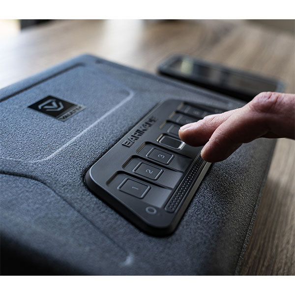 Hand tippt auf Zahlentastatur eines Safes in Innenraum auf Holztisch.