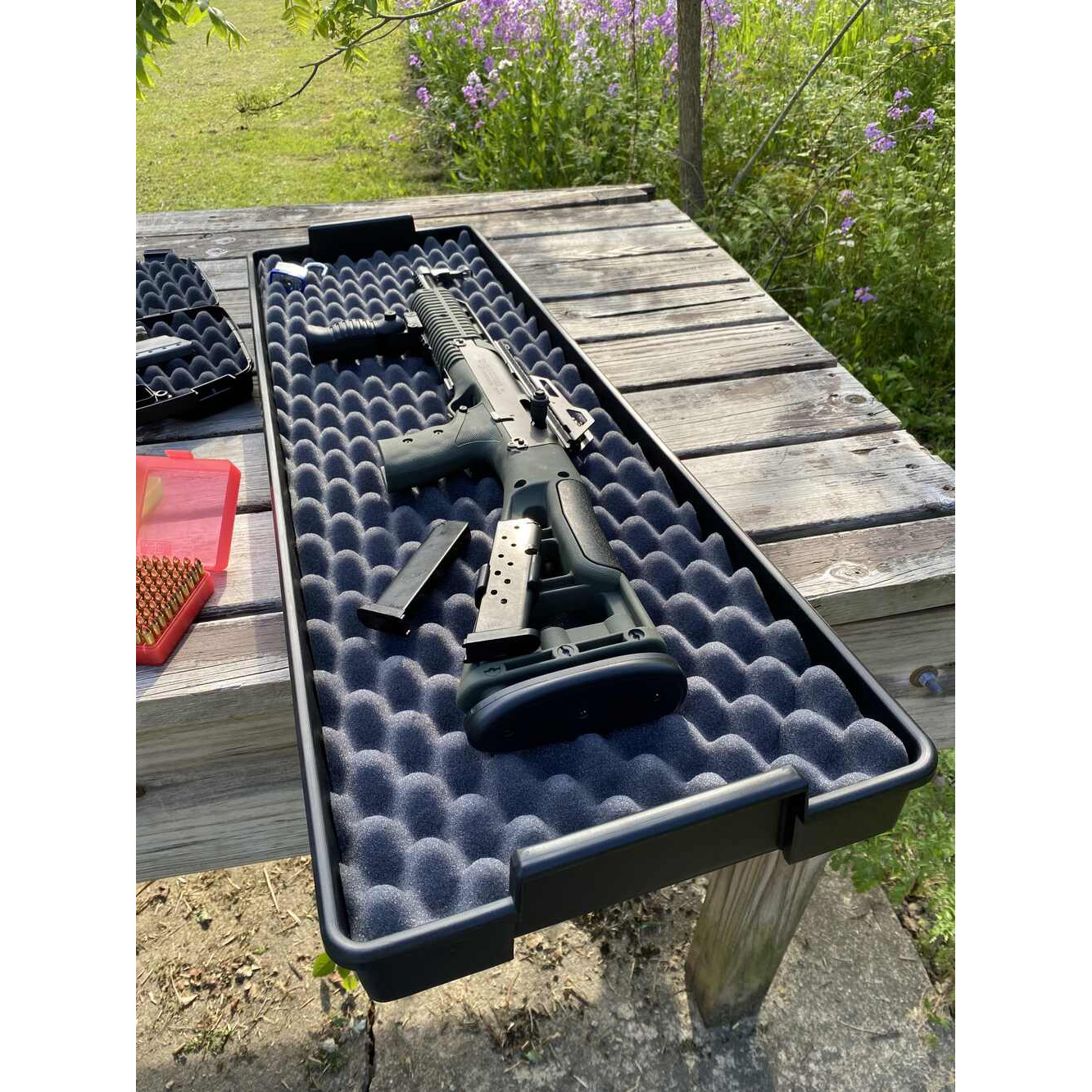 Ein Gewehr liegt in einem gepolsterten Koffer auf einem Holztisch im Freien.
