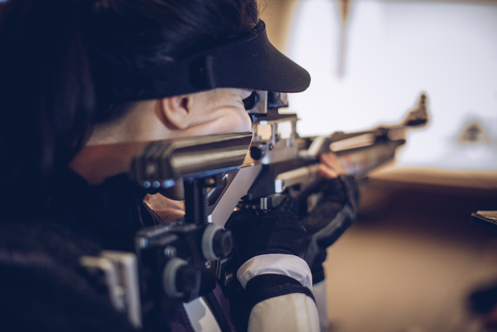 Sportschuetzin in Schiessausruestung mit Gewehr in Anschlagposition.