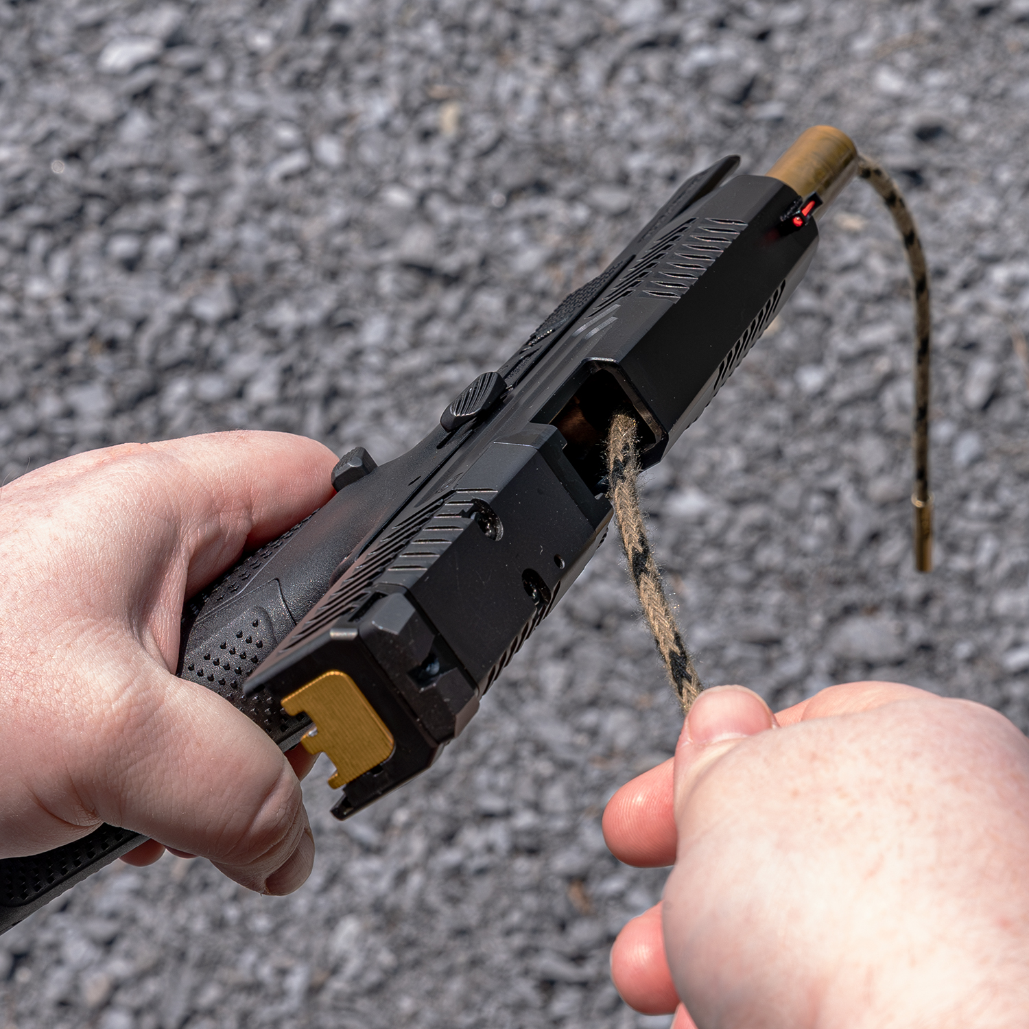 Eine Pistole wird mit einem Reinigungstuch in einer kiesigen Umgebung gereinigt.