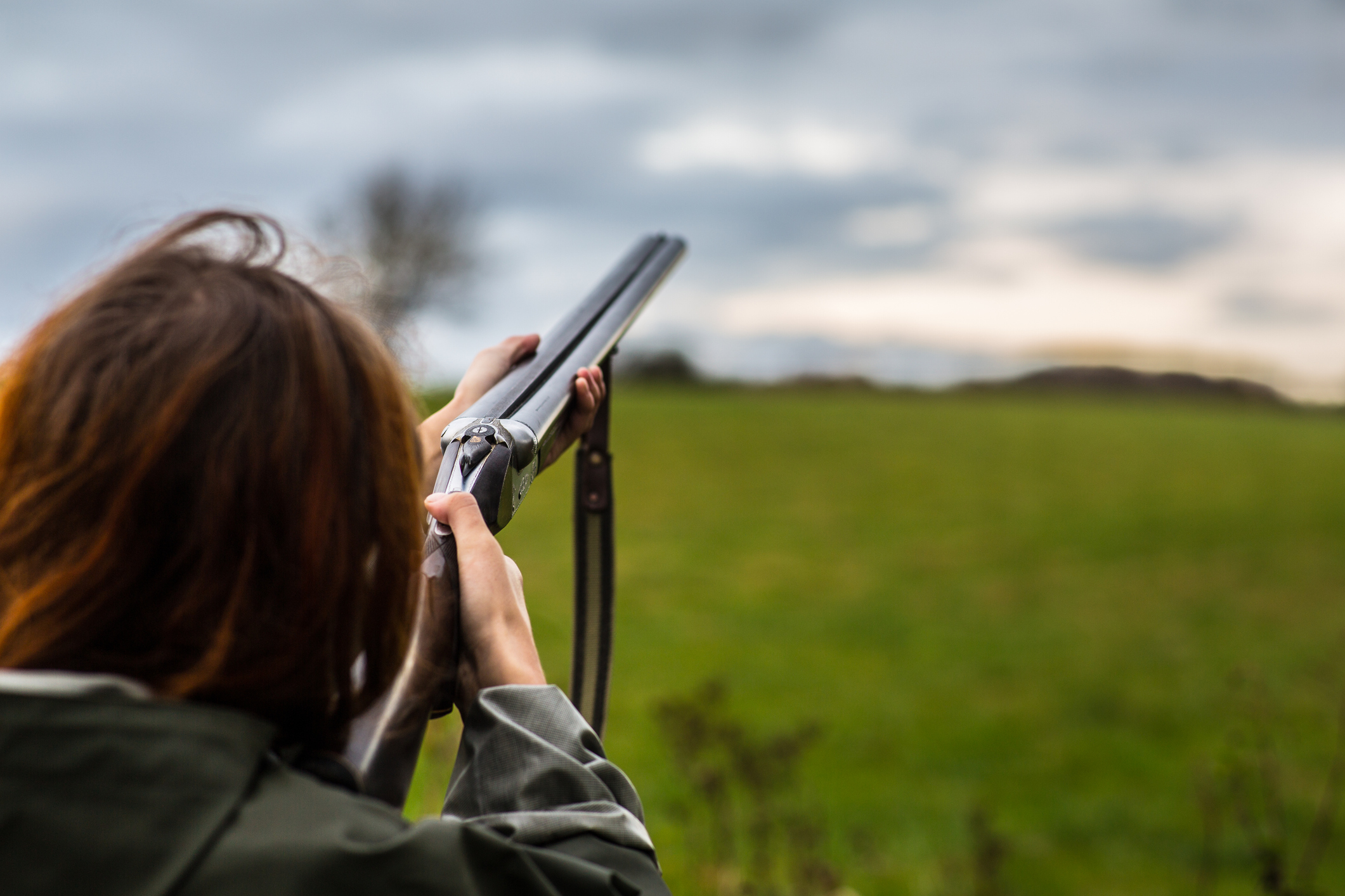 Person mit Doppelflinte beim Zielen auf einer offenen Wiese.