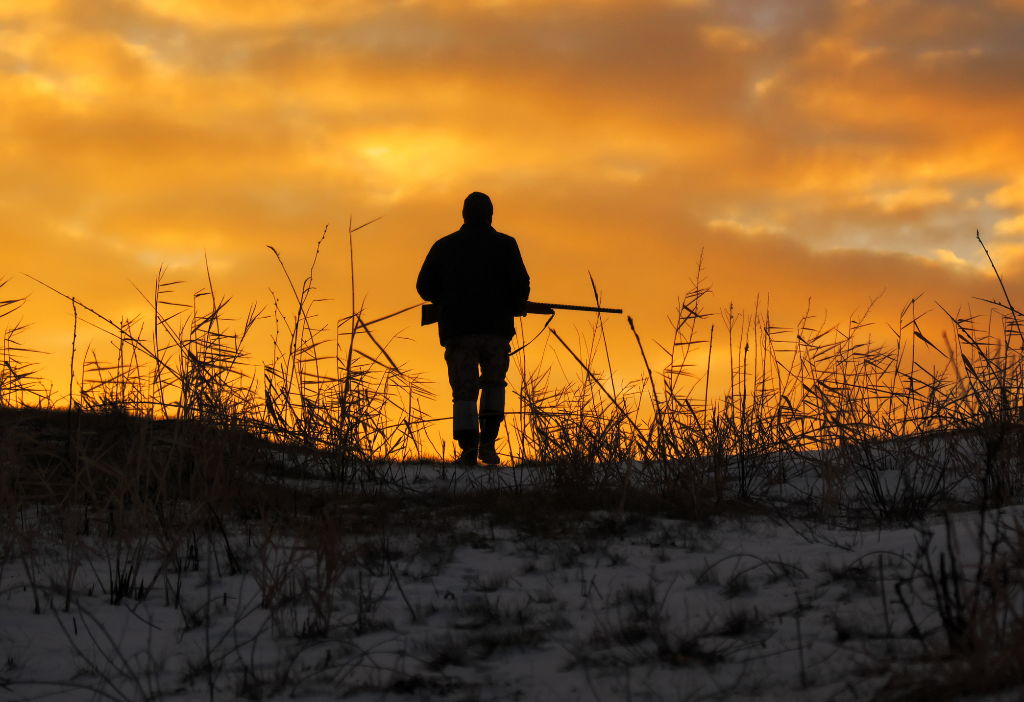 Person mit Gewehr steht auf sandigem Hügel vor orangefarbenem Himmel