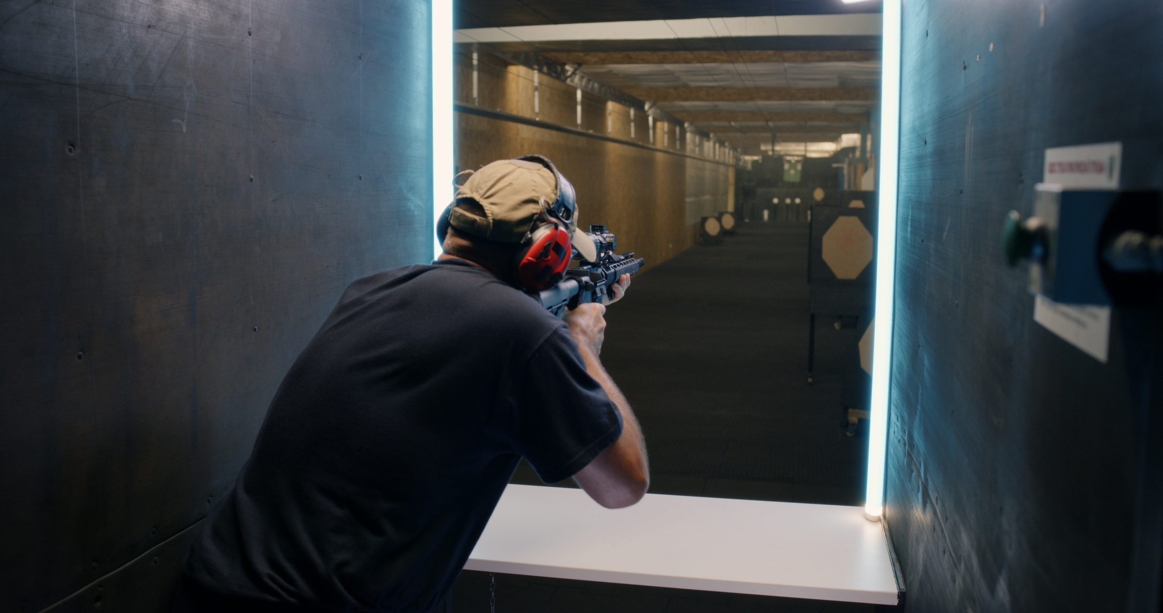 Person mit Gehörschutz zielt mit einem Gewehr auf Zielscheiben im Schiessstand.