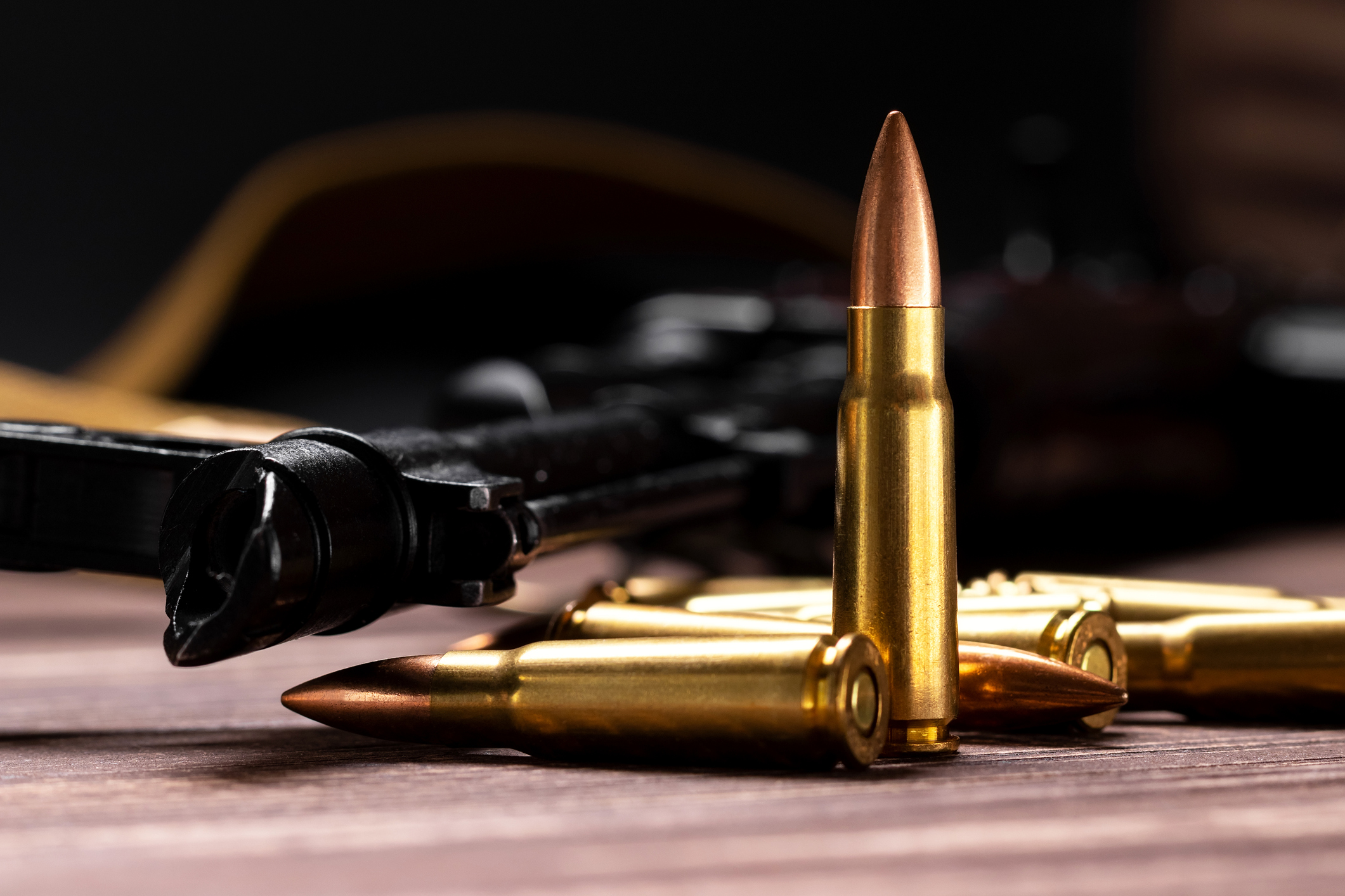 Gewehrpatronen auf Holztisch, im Hintergrund unscharfe Schusswaffe.