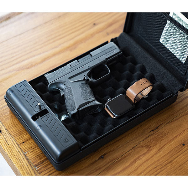 Pistole und Armbanduhr liegen in einem Schaumstoffkoffer auf einem Holztisch.
